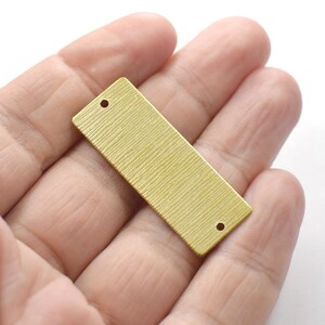 May include: A gold-colored rectangular metal tag with two holes. The tag has a textured surface.