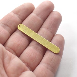 May include: A gold-colored metal bar with a hole at the top. The bar has a brushed finish and is about 2 inches long.