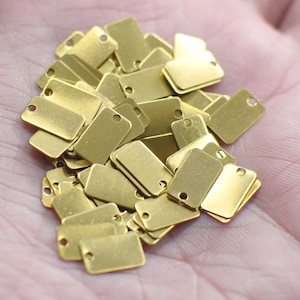 Può includere: Un mucchio di piccoli cartellini rettangolari in ottone con un foro in ciascuno. I cartellini sono tutti della stessa dimensione e forma, e sono disposti in ordine casuale.