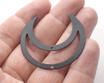 Könnte beinhalten: Zwei schwarze Halbmondformen aus Metall, eine in der anderen, mit kleinen Löchern zum Aufhängen. Die Monde werden in einer Hand vor weißem Hintergrund gehalten. Der äußere Mond hat einen Durchmesser von etwa 5 cm.