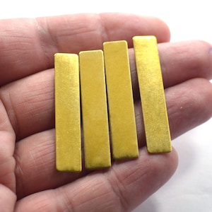 Pode incluir: Quatro barras de metal de cor dourada, cada uma com uma superfície lisa ligeiramente texturizada. As barras estão dispostas em fila, com a barra mais longa na parte superior e a barra mais curta na parte inferior.