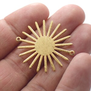 May include: Gold-toned metal sunburst charm with two jump rings. The charm has a textured surface and a circular center.
