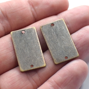 May include: Two antique gold-toned metal rectangular tags with two holes each. The tags are blank and ready for personalization.