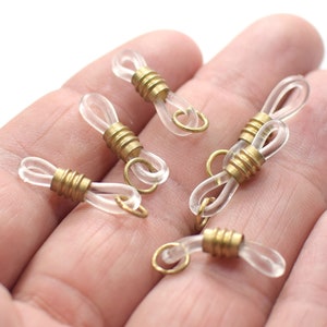 Puede incluir: Cinco porta-cadenas de gafas de plástico transparente con cierres de metal dorado. Los cierres tienen un diseño estriado.