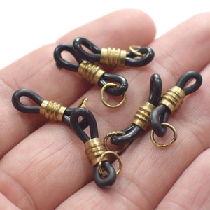Puede incluir: Cinco conectores de cadena de gafas en negro y dorado. Cada conector tiene un anillo de metal dorado en un extremo y un bucle de goma negro en el otro extremo.