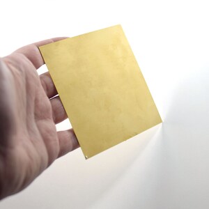 Könnte beinhalten: Ein Blatt aus Messingblech, goldfarben, wird von einer Hand gehalten. Das Metall ist glatt und glänzend.