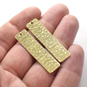 May include: Two gold-colored metal rectangular tags with a hammered texture and a hole at the top.