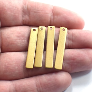 May include: Five gold-colored metal bar pendants with a hole at the top. The pendants are arranged in a row, with the hole at the top of each pendant facing the viewer.