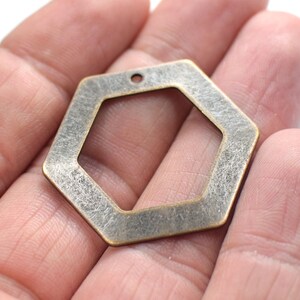 May include: A hexagonal metal charm with an antique brass finish. The charm has a hole at the top for attaching to a necklace or bracelet.