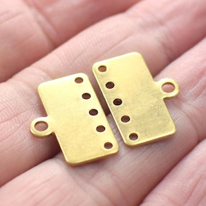 May include: Two gold metal clasps with multiple holes for attaching jewelry or other crafts. The clasps have a loop on one end for attaching to a chain or cord.