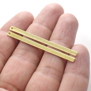 May include: Two gold-coloured metal bars with rounded ends and small holes at each end. The bars are lying on top of each other.