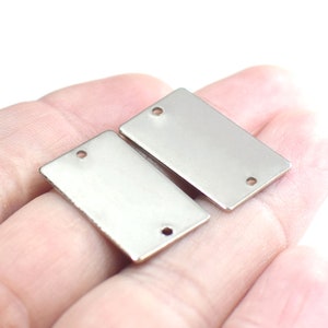 Pode incluir: Duas etiquetas retangulares de metal prateado com dois furos cada. As etiquetas estão em branco e prontas para serem personalizadas.