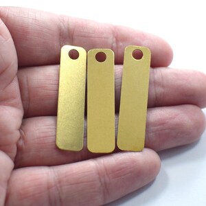 May include: Three gold-colored metal tags with rounded edges and a hole at the top. The tags are arranged in a row.