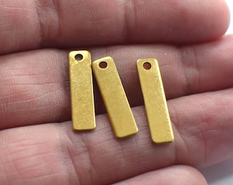 May include: Three gold-colored metal rectangular tags with a hole at the top. The tags are on a hand.