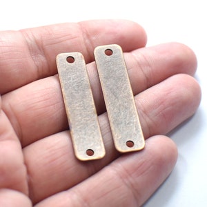 Pode incluir: Duas etiquetas retangulares de metal com acabamento dourado antigo, com dois furos cada. As etiquetas medem aproximadamente 3,8 cm de comprimento e 1,3 cm de largura.