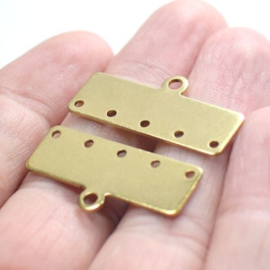 Op de afbeelding: Twee goudkleurige metalen connectorstukken met meerdere gaten om sieraden of andere knutselwerkjes aan te bevestigen. Elk stuk heeft een lus aan de bovenkant om aan een ketting of koord te bevestigen.