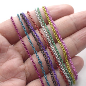 Puede incluir: Surtido de cadenas metálicas de colores en varios colores, incluyendo azul verdoso, morado, negro, rojo, plateado y verde. Las cadenas están dispuestas en forma de abanico en una mano.