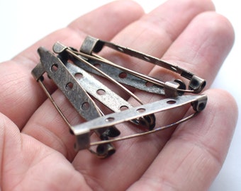 Puede incluir: Primer plano de un montón de cinco cierres de seguridad de metal de estilo antiguo. Los pasadores son de color bronce oscuro y tienen un diseño decorativo.