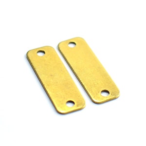 Op de afbeelding: Twee rechthoekige metalen labels in goudkleur met afgeronde hoeken en een gat aan elk uiteinde.