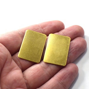 May include: Two gold-colored rectangular metal pieces, possibly jewelry, are held in a hand.