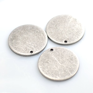 Op de afbeelding: Drie zilverkleurige metalen cirkels met een verweerde afwerking en een klein gaatje in het midden.