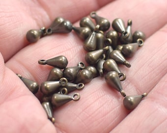 May include: A pile of antique gold-toned teardrop-shaped metal charms with a loop at the top for attaching to jewelry or other crafts.
