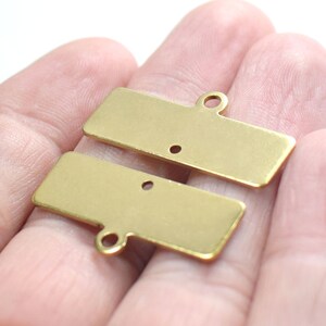 May include: Two gold-colored metal rectangular tags with a hole in each. The tags are stacked on top of each other.