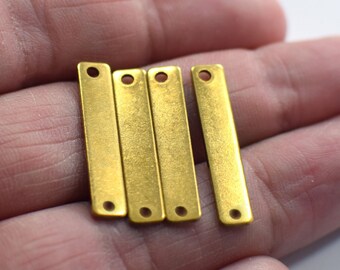 May include: Four gold-colored metal bar charms with two holes each. The charms are arranged in a row and are about 1 inch long.