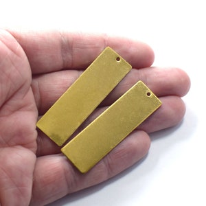 May include: Two gold-colored metal rectangular tags with a hole punched at the top. The tags are about 2 inches long and 1 inch wide.
