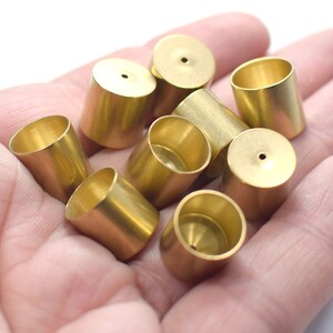 May include: A group of eight gold-coloured metal caps with a small hole in the top. The caps are cylindrical and have a smooth, shiny finish.