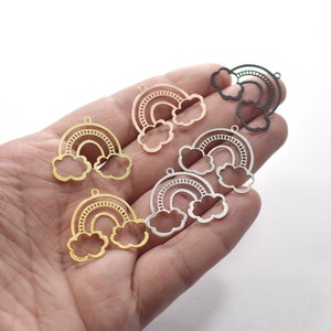 Könnte beinhalten: Fünf Regenbogen-Anhänger in verschiedenen Metalloberflächen: Gold, Silber, Roségold und Schwarz. Jeder Anhänger zeigt einen Regenbogen mit zwei Wolken.
