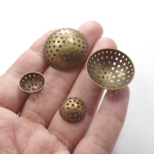 Könnte beinhalten: Vier kupferfarbene, kuppelförmige Metallembellishments mit einem perforierten Design. Die Kuppeln sind in verschiedenen Größen und auf einer Hand angeordnet.