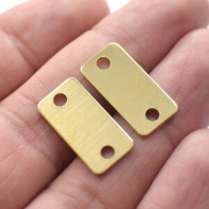 Pode incluir: Duas etiquetas retangulares de metal de cor dourada com dois furos cada. As etiquetas são lisas e têm um acabamento escovado.