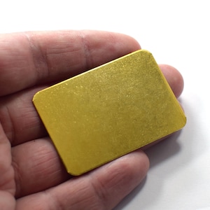 Puede incluir: Una pequeña placa rectangular de metal de color dorado.