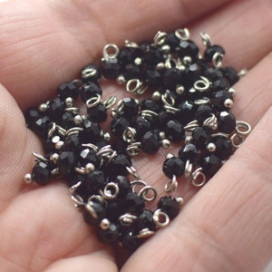 May include: A close-up of a pile of black crystal beads with silver jump rings. The beads are faceted and have a shiny finish.