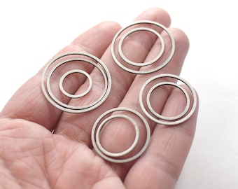 May include: Four silver metal rings of different sizes, with one ring nested inside another, are displayed on a hand.