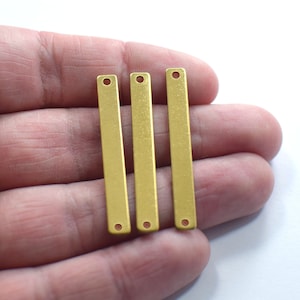 May include: Three gold-colored metal bar pendants with two holes each. The bars are flat and have a smooth, brushed finish.