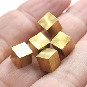 May include: Five small, gold-coloured, cube-shaped metal pieces are arranged in a cluster on a person's hand.