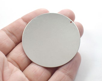 May include: A silver round metal disc with a small hole in the top. The disc is smooth and has a shiny finish.