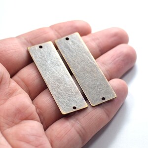 Op de afbeelding: Twee rechthoekige metalen blanco's van antiek messing met gaten om op te hangen. De blanco's hebben een geborstelde afwerking.