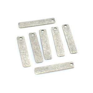 May include: Seven silver-toned metal rectangular tags with a hole at the top. The tags have a distressed, aged look.