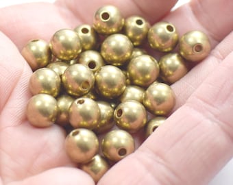 May include: A pile of gold-colored round beads in a hand. The beads are smooth and have a hole in the center.