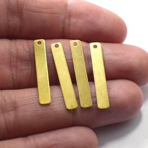 May include: Four gold-coloured metal bar pendants with a hole at the top. The pendants are approximately 2.5 cm long and have a brushed finish.
