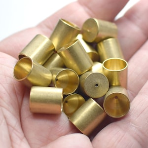 May include: A close-up of a hand holding a pile of brass caps. The caps are all the same size and shape, and they have a shiny, metallic finish.
