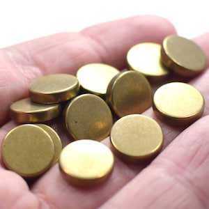 May include: A pile of round, brass-colored metal discs, approximately 1 inch in diameter, are displayed in a hand.