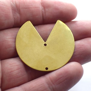 Könnte beinhalten: Ein goldfarbener Metallanhänger in Form eines Halbkreises mit einem V-förmigen Ausschnitt. Der Anhänger hat zwei Löcher zum Anbringen einer Kette oder Schnur.