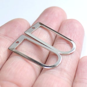 May include: Two silver-toned metal earring findings with a rectangular shape and a small hole at the top. The findings are designed to be used for attaching earrings to jewelry.