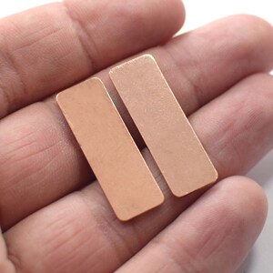 May include: Two rectangular copper-colored metal sheets, held in a hand.