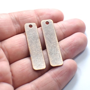May include: Two antique gold-toned metal rectangular tags with a hole at the top. The tags are slightly textured and have a worn look.