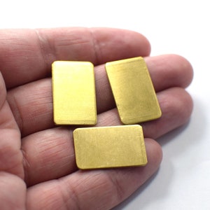 May include: Three gold-colored rectangular metal pieces, possibly brass, are held in a hand. The pieces are smooth and have a slightly textured surface.